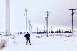 Man in heavy jacket stands in front of large array of wind turbines