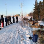 Ambler residents look on as Nicolas Petit gets his dogs settled in straw on the snow at the checkpoint.