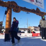 2016-2018 KNOM Volunteer Karen Trop poses at the Iditarod Finish Line in Nome, 2018.