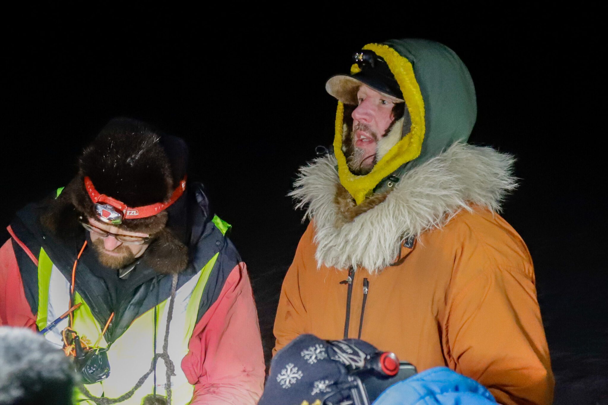 A musher in an orange jacket