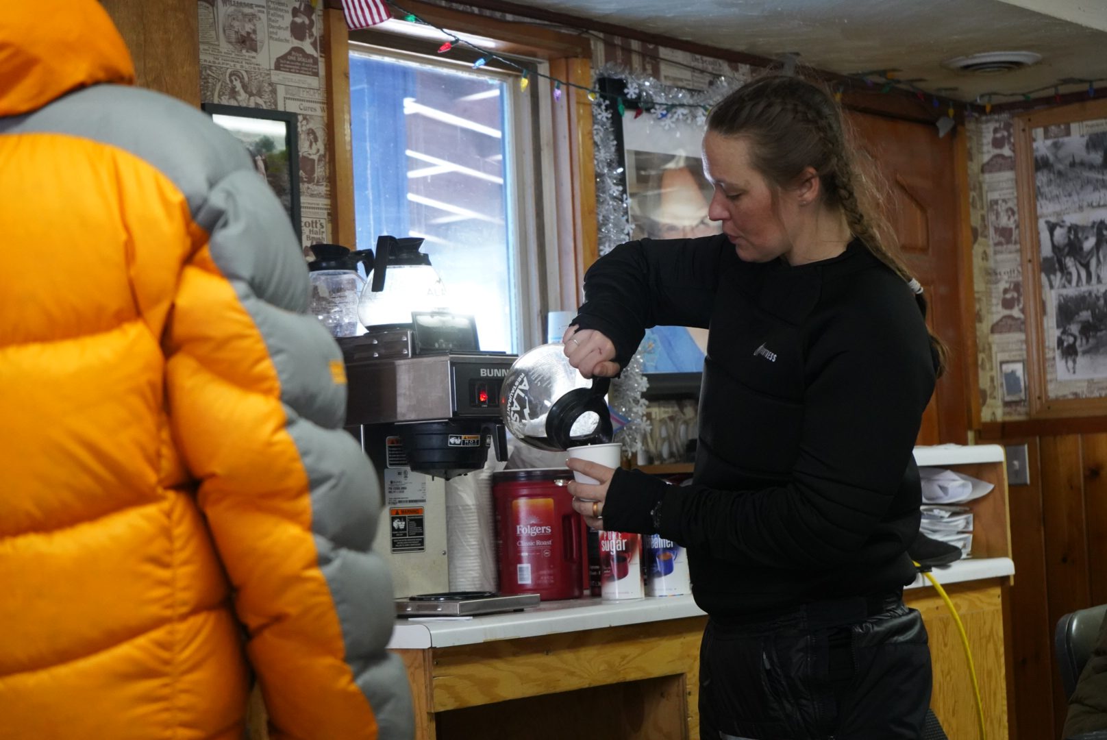 A woman with braids wearing black pours herself a cup of coffee