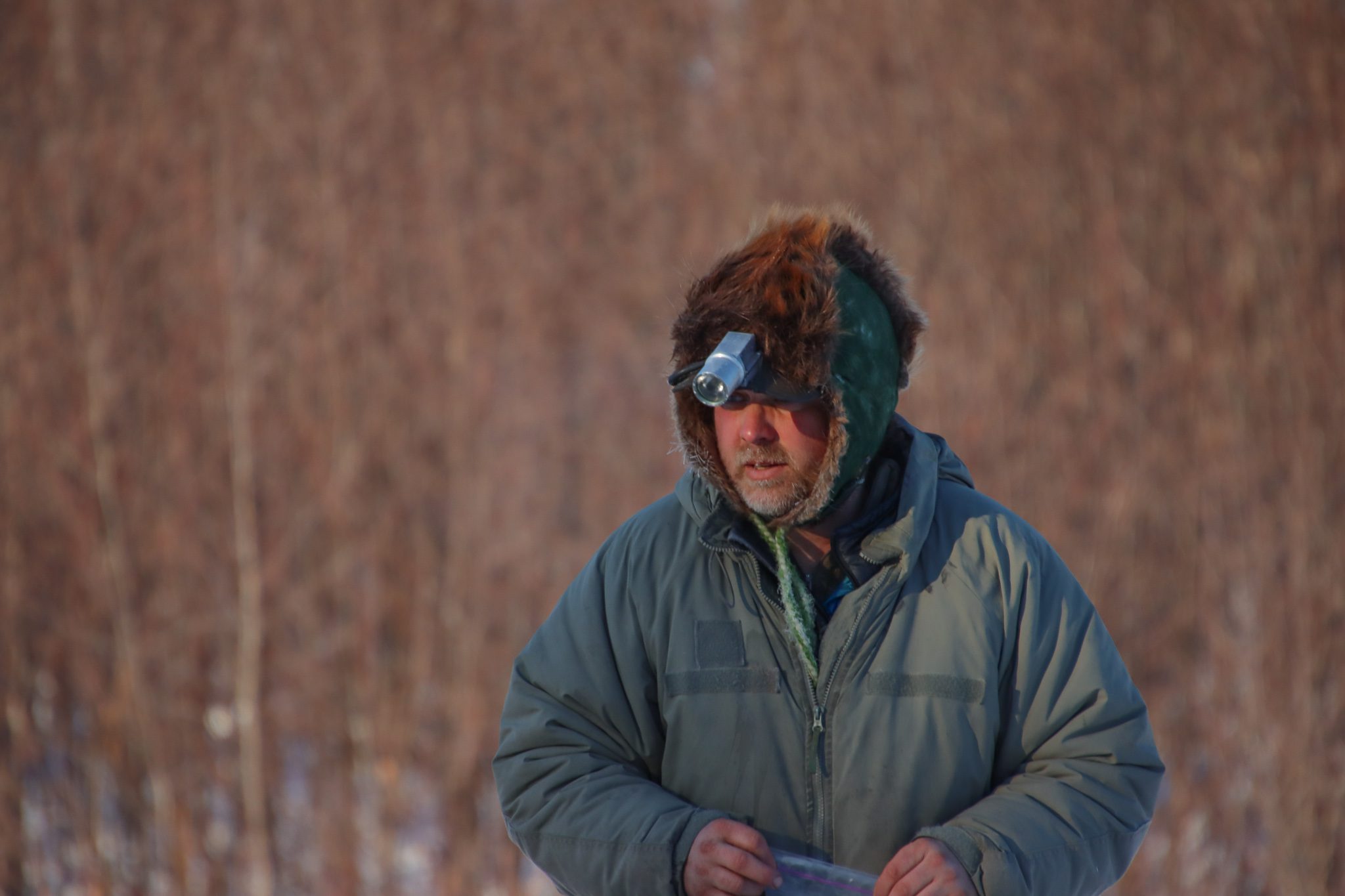 A man in a fur hat and a grey-green jacket looks down