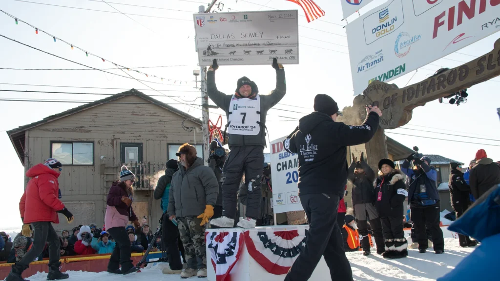 2024 Iditarod Champion, Dallas Seavey, holds an oversized check above his head as the crowd on Front Street celebrates his victory. (Ben Townsend photo)