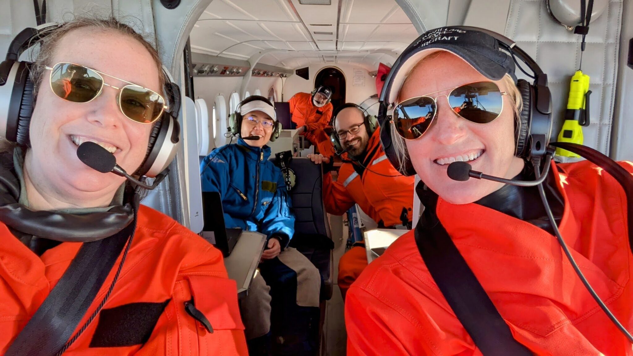 Lt. Cmdr. Denise Miller, left, and Lt. Laura Rock, right, take a selfie from the cockpit of the Twin Otter aircraft. Jiaxu Zhang, John Kucewicz, and Brenton Salmi sit in the cabin. Photo courtesy of Arctic AIR. 