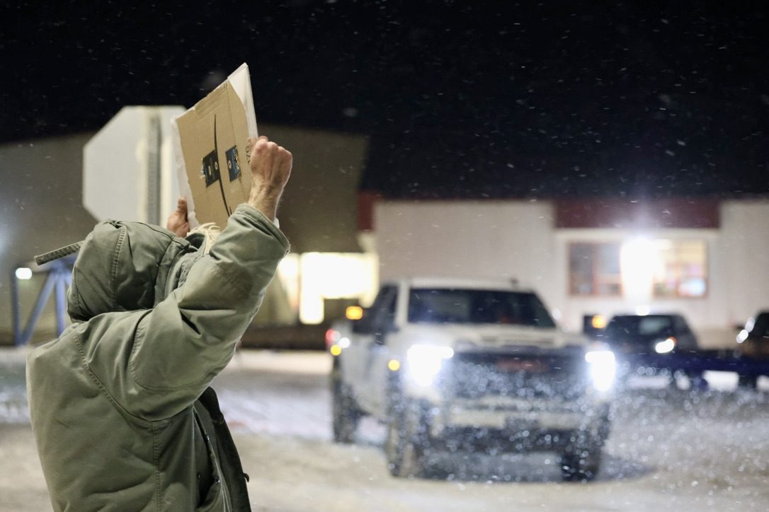 A truck exits the Nome Elementary School parking lot as a picketer holds a sign above his head. Ben Townsend photo.