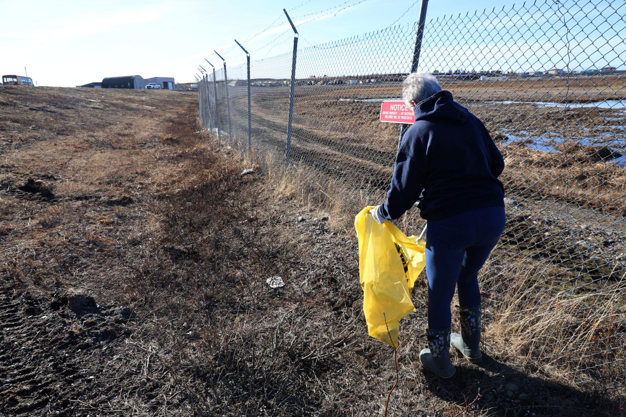 977A9178 copy Mary Reader scoops trash with a handheld picker along the fence line of the Nome Airport. Laura Davis Collins photo.