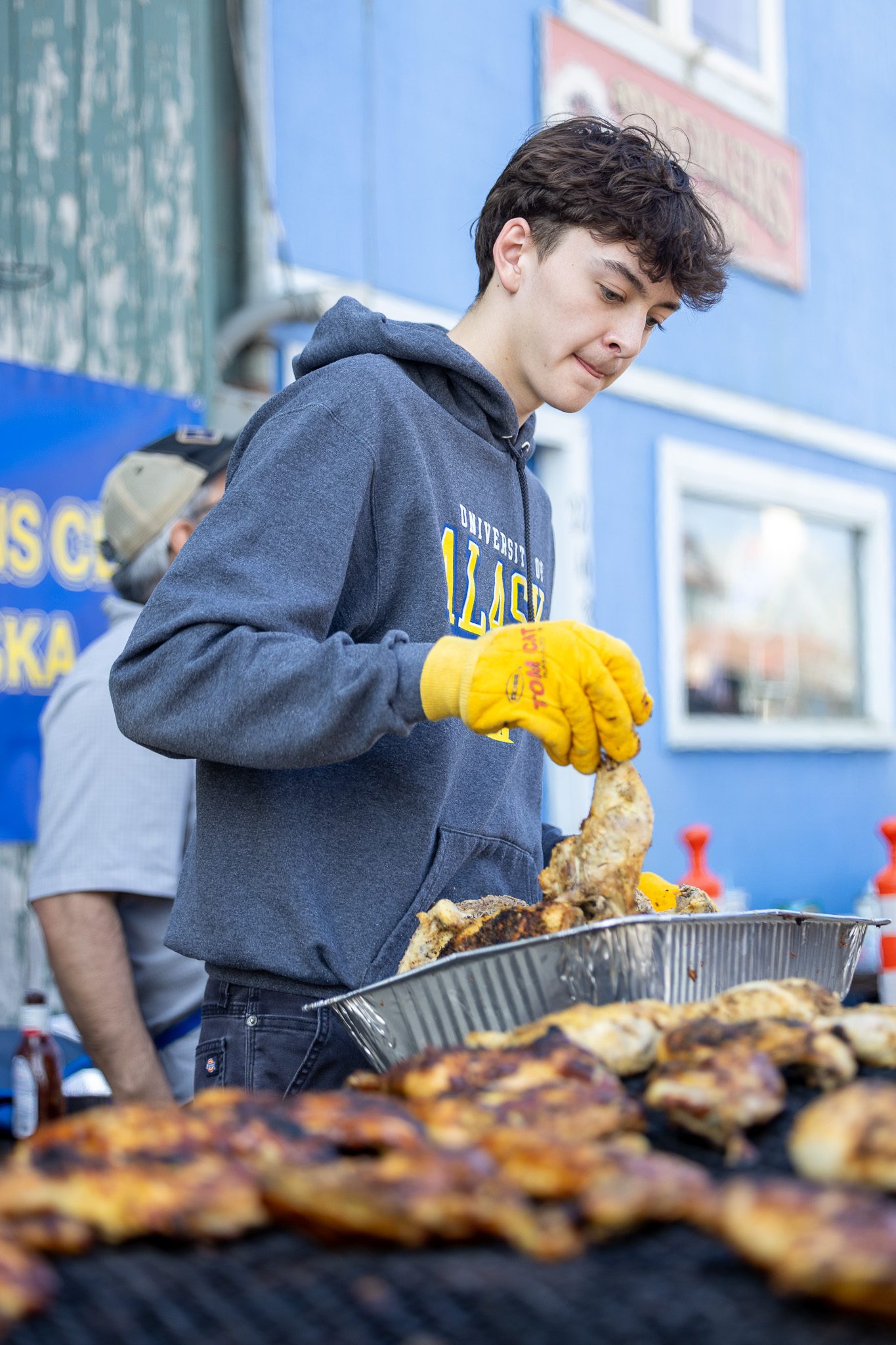 102A4482 Cohen Booth prepares to place a chicken on a grill at Bering Sea Lion's Club's Chicken Feed event. Ben Townsend photo.