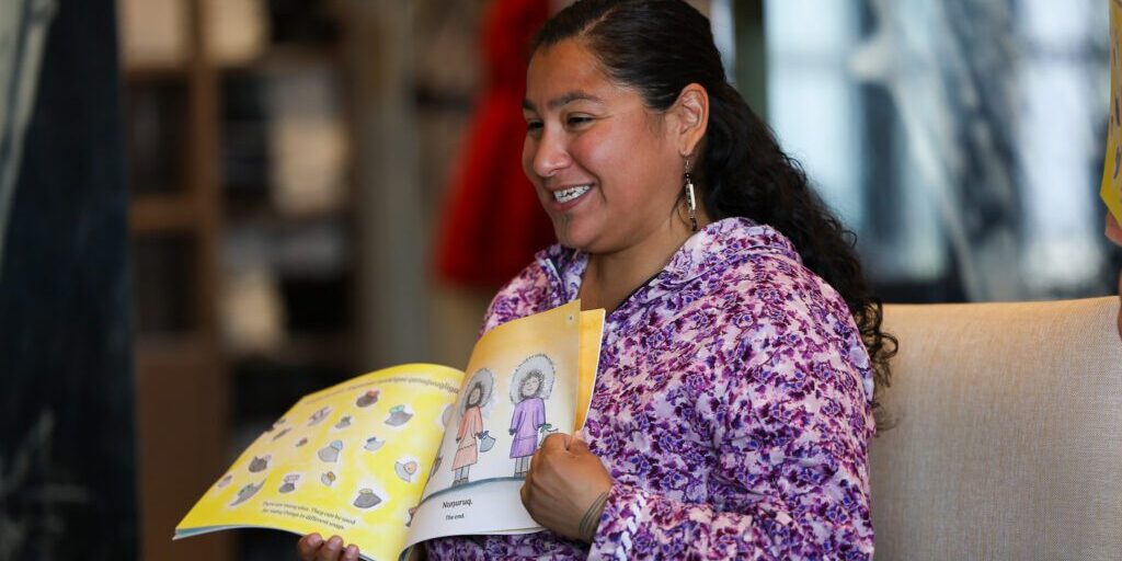 Kunaq Tahbone looks toward children gathered on the ground while reading her book, “Uluit Atuqtaatka”. Ben Townsend photo.