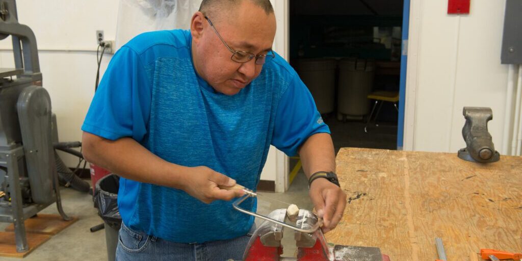 Jerome Saclamana shows students how to saw ivory. Photo: Mitch Borden, KNOM.