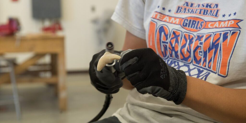 Ivory shaping her fish carving with a dremel. Photo: Mitch Borden, KNOM.