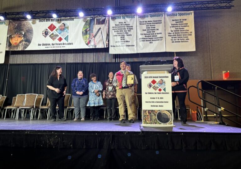 Barret Eningowuk stands on stage with a plaque and flowers at the Alaska Federation of Natives conference. Janice Homekingkeo photo. 