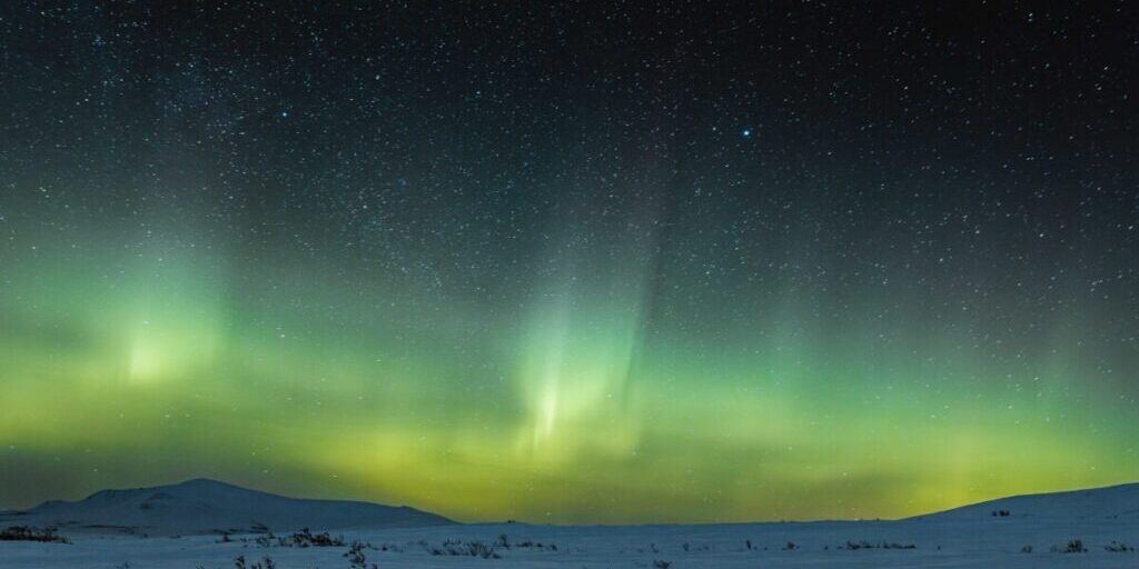 An aurora borealis hovers over the hills behind Nome in March 2024. Michael King photo used with permission.